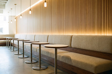 Restaurant banquette in oatmeal fabric on a walnut base against a lit oak slat wall