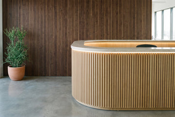 Curved reception desk in white oak slats with a stone top in front of a walnut slat wall