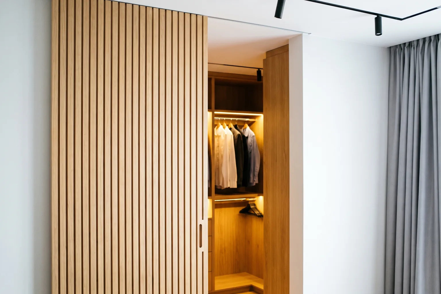 White oak slat sliding door on a concealed track opening into a lit walk-in closet